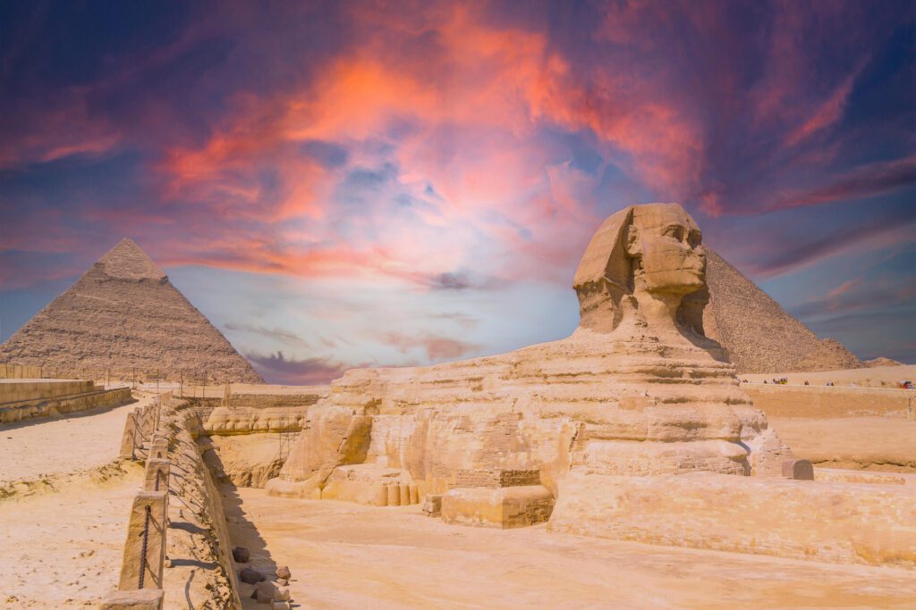 View of the the Great Sphinx and the Pyramids of Giza against a colorful sunset at Giza, Egypt